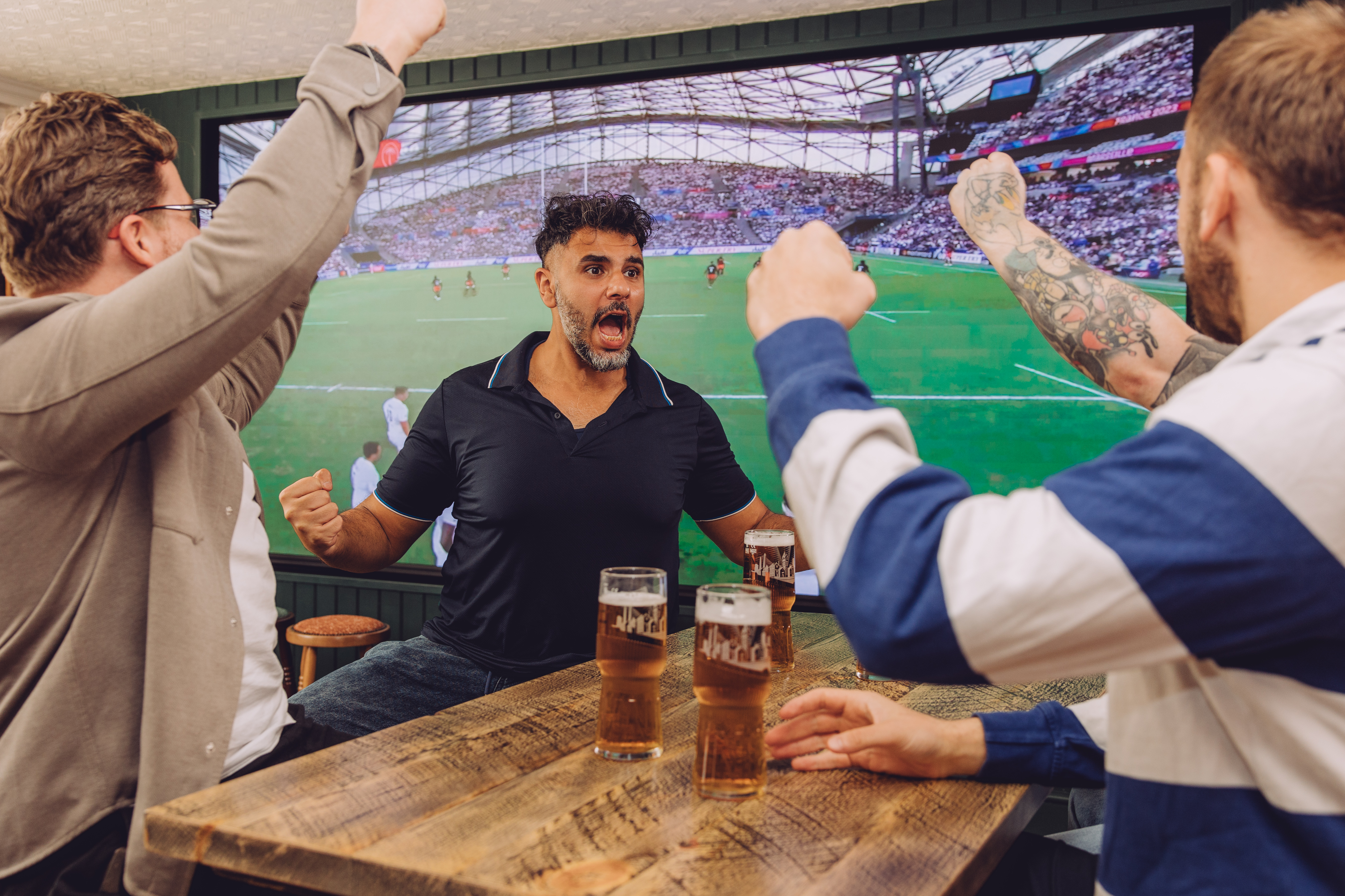 Excited patrons cheer at a Cottingham pub, watching a live sports match on a large screen while enjoying drinks.