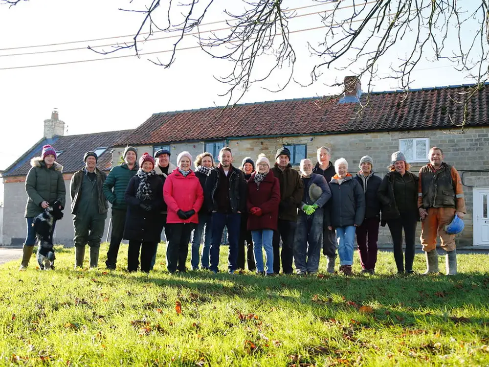 Group of volunteers standing together in front of The Plough pub in Fadmoor, surrounded by green grass and trees.