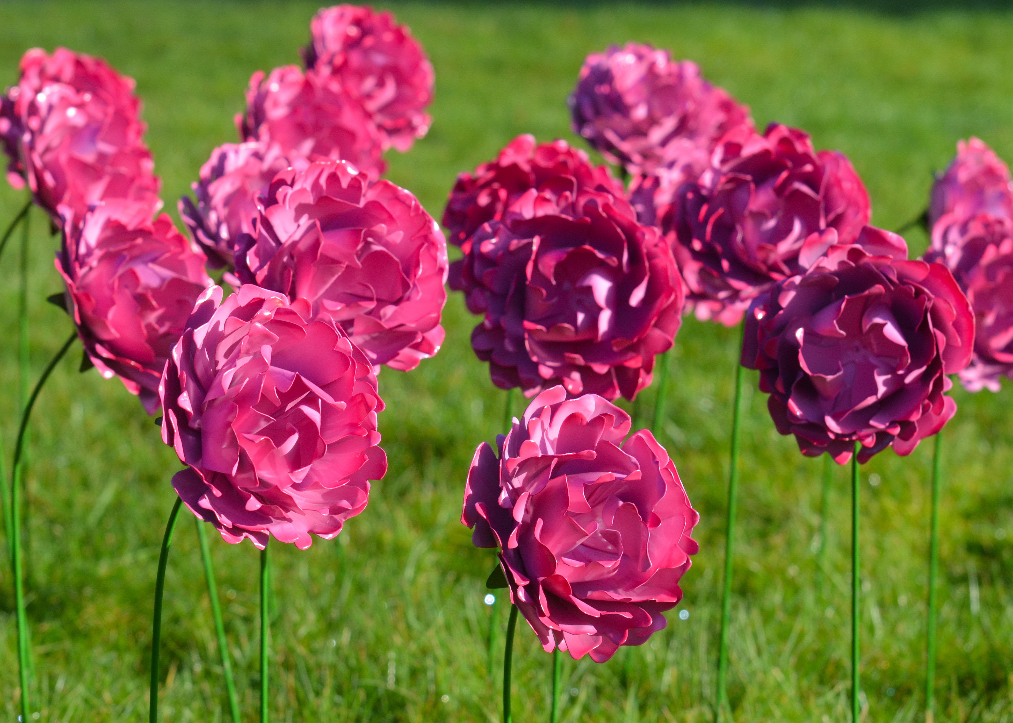 Vibrant pink paper flowers stand tall on green grass, creating a cheerful atmosphere for Mother's Day celebrations.
