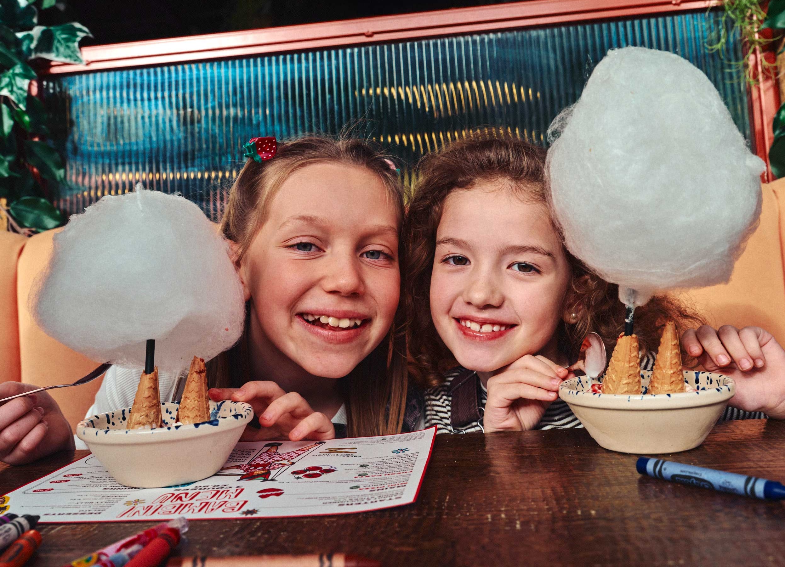Two smiling children enjoying cotton candy in a cozy cafe