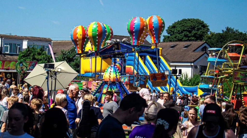 Brightly colored carnival rides with inflatable hot air balloons, lively crowds enjoying a summer festival atmosphere.