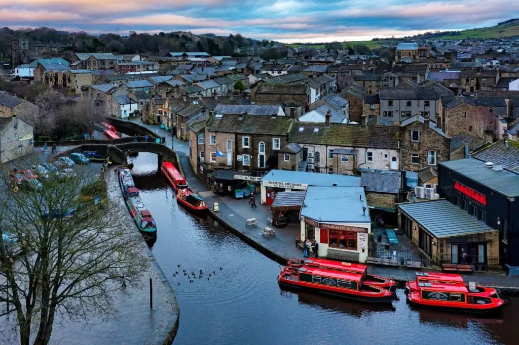 A scenic view of a canal surrounded by quaint buildings and colorful boats under a cloudy sky in Yorkshire.