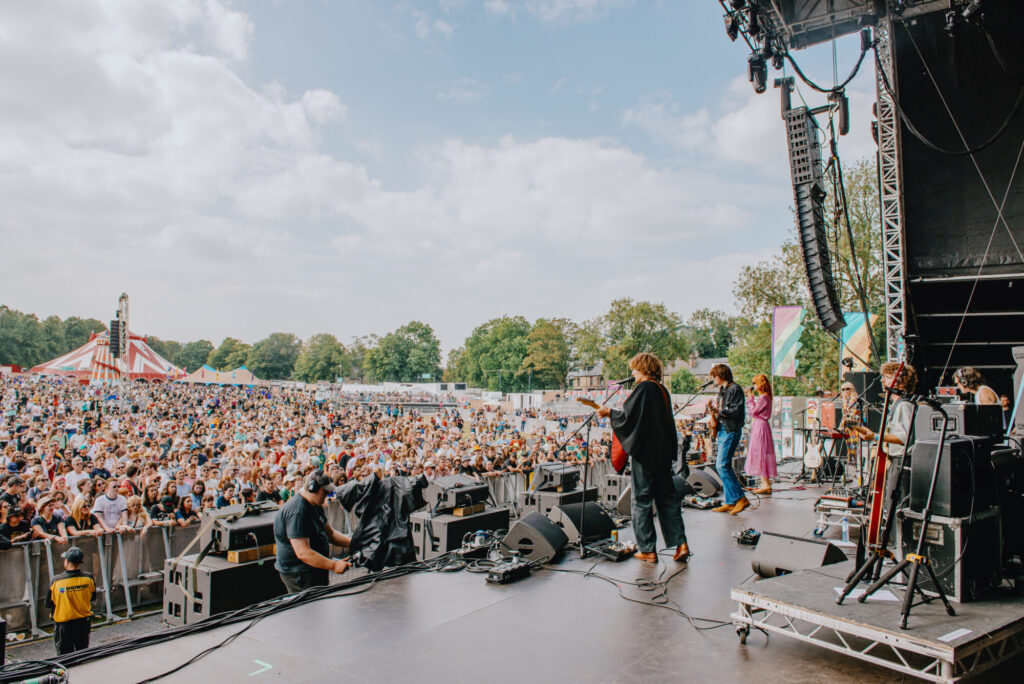 Vibrant festival scene with diverse crowd enjoying live music on stage under a cloudy sky in Sheffield.