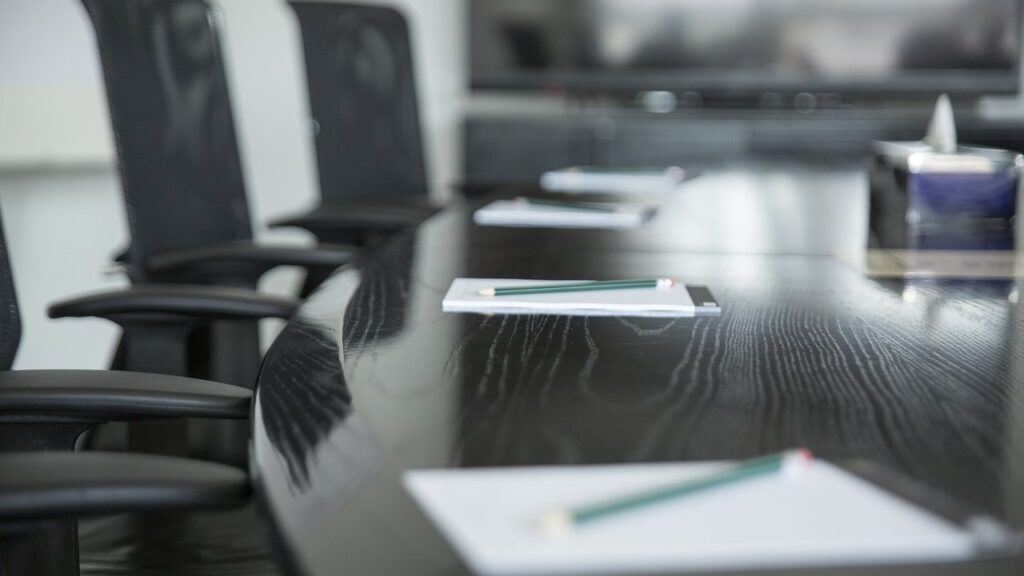 Boardroom setting with a long black table, empty chairs, and stationery, suggesting a professional meeting space.