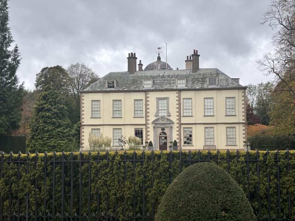 Elegant Myton Hall features a symmetrical facade, large windows, and lush greenery against a cloudy sky.