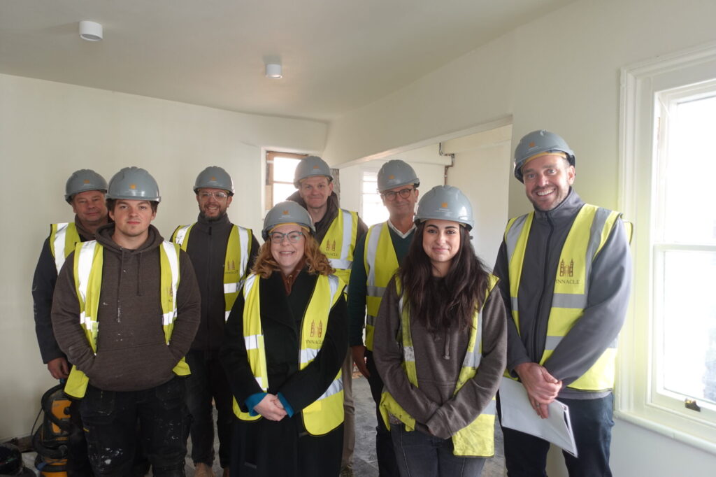 A group of people in hard hats and reflective vests poses in a bright, unfinished room, showcasing teamwork in conservation.
