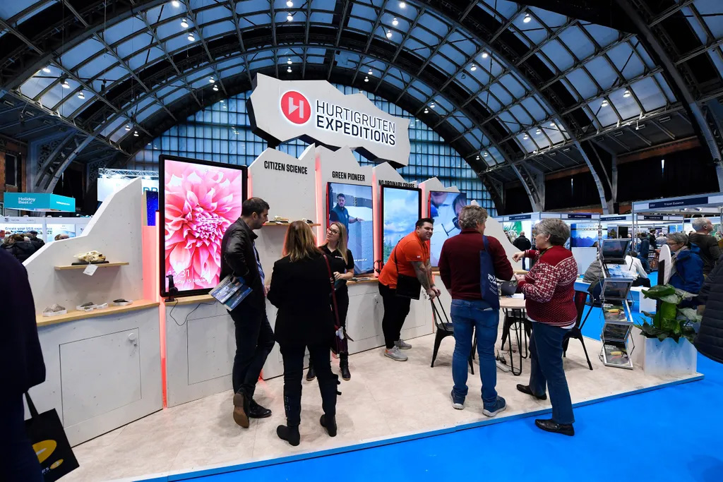 Exhibition booth featuring interactive screens, engaging visitors, and travel displays in a spacious convention hall.