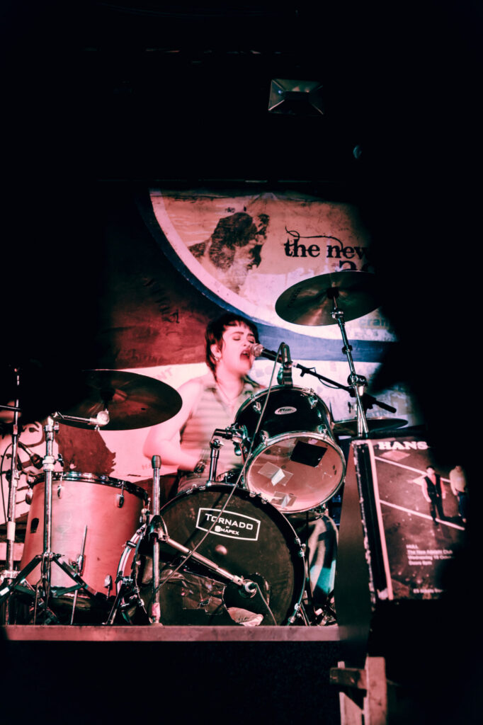 A drummer passionately performing on stage, surrounded by vibrant lighting and a colorful backdrop.