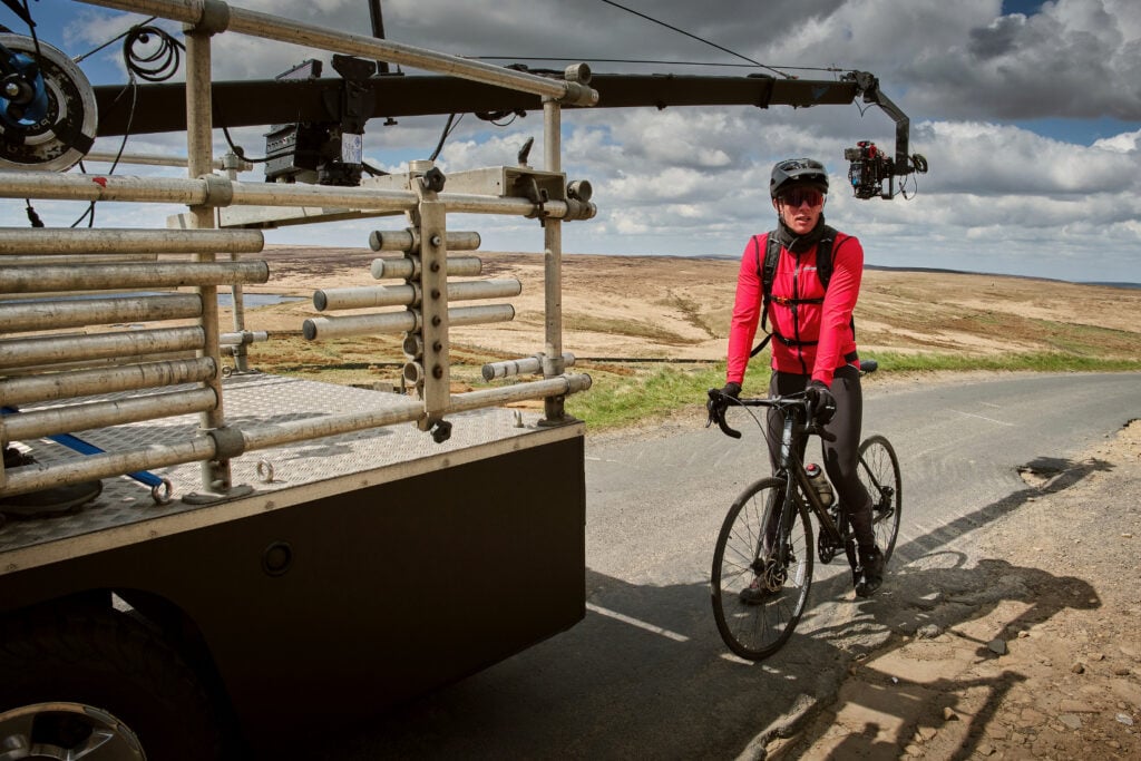 James Norton as Tommy Lee Royce in Happy Valley 3, filming behind the scenes in cycling outfit above Warley Moor reservoir with bike